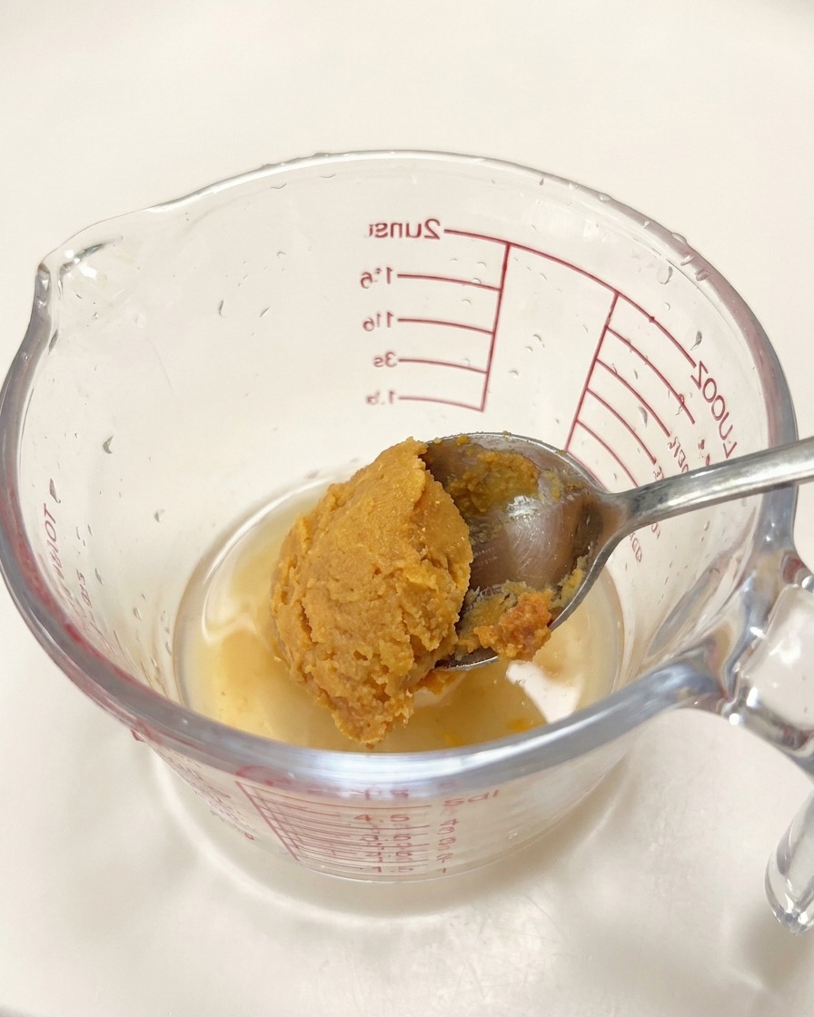 Une cuillère de pâte miso ajoutée à un verre doseur contenant les assaisonnements liquides.