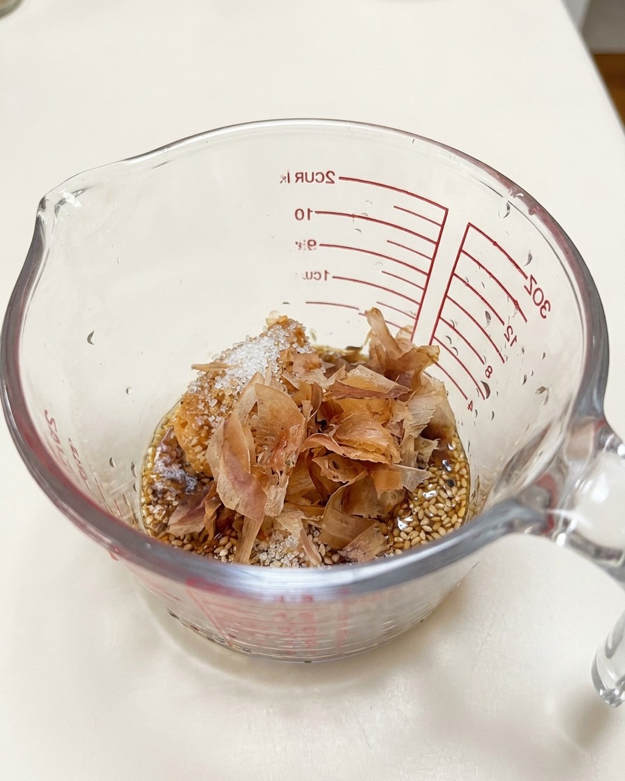 Flocons de bonite déposés sur la pâte miso et les graines de sésame dans un verre doseur.
