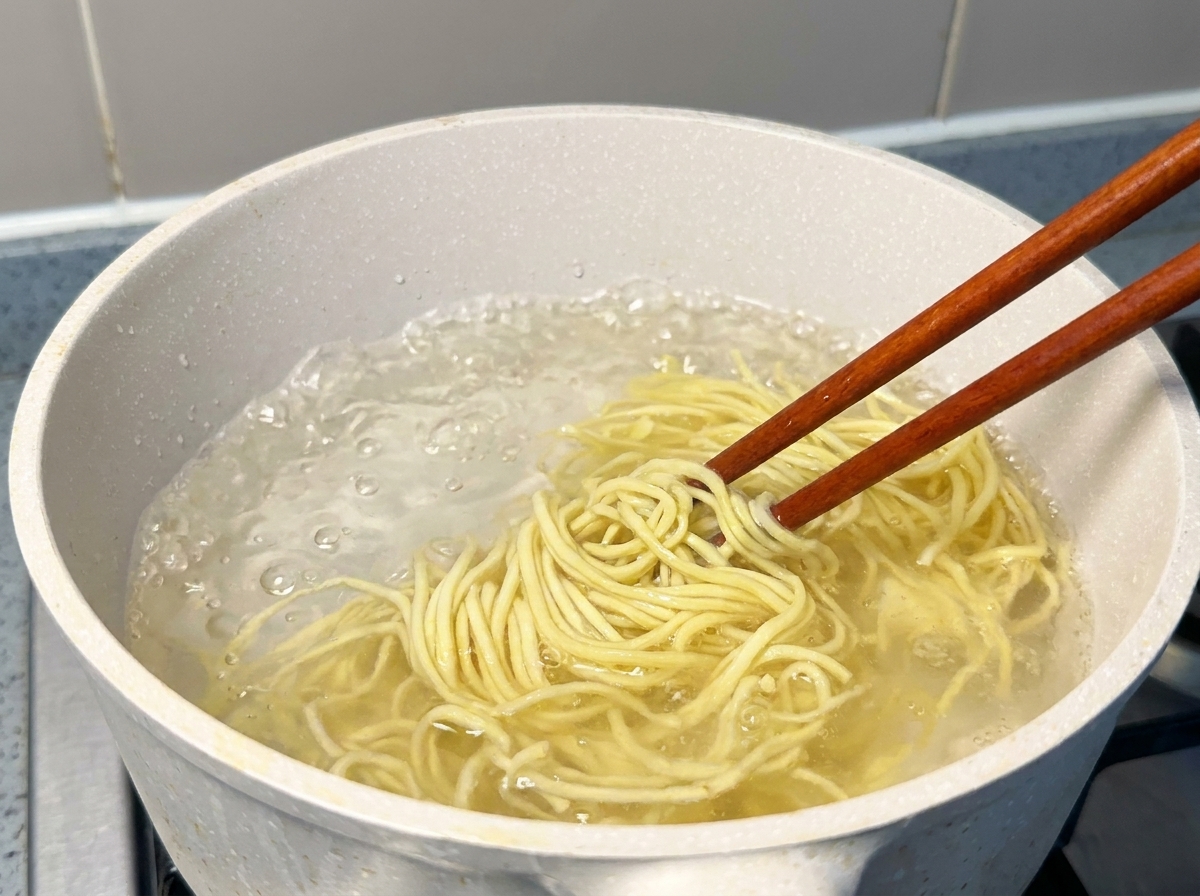 Nouilles ramen jaunes soulevées avec des baguettes dune casserole deau bouillante.