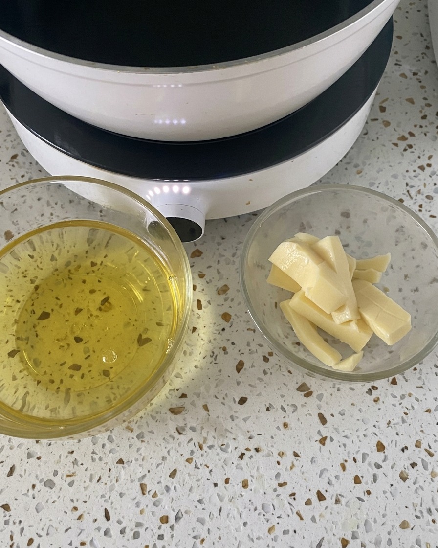 Deux petits bols en verre contenant des œufs cassés et des tranches de mozzarella sur un plan de travail blanc à côté dune plaque chauffante.