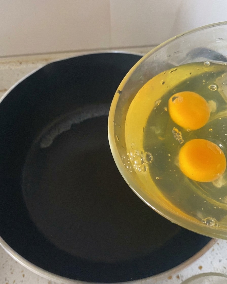 Deux œufs crus versés dun bol en verre dans une poêle sombre et chaude.