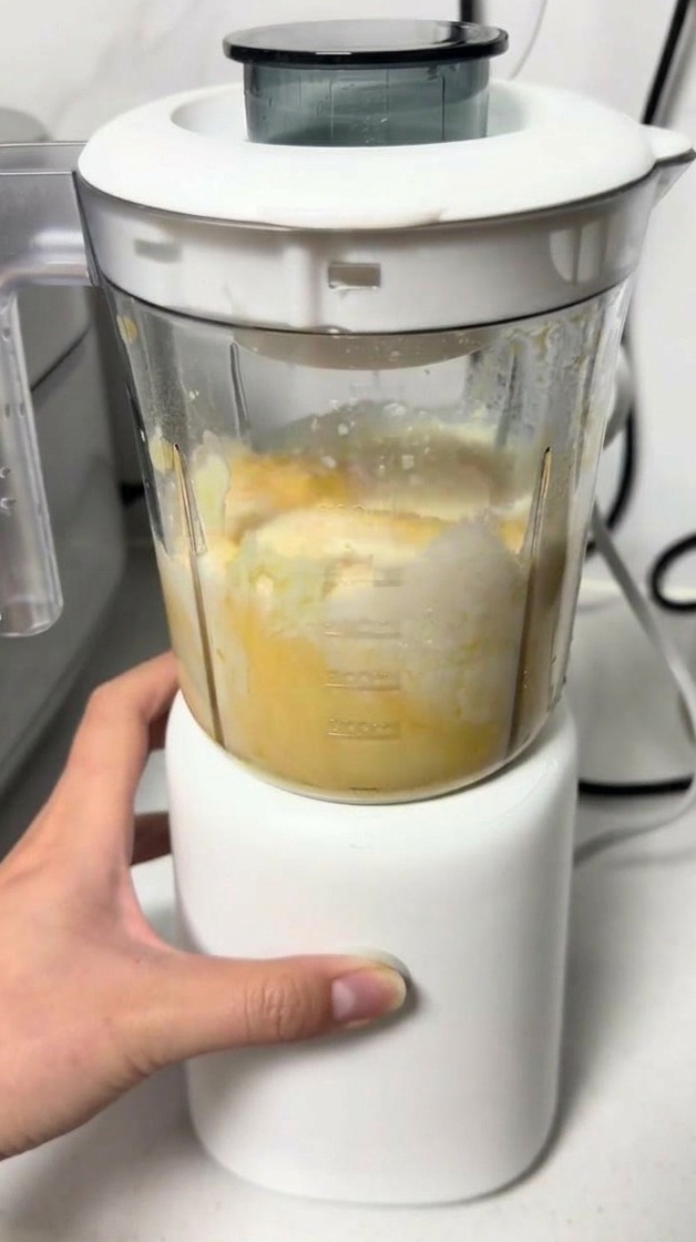 Une main actionnant un petit blender blanc en train de mixer une pâte jaune vif à lintérieur du récipient.