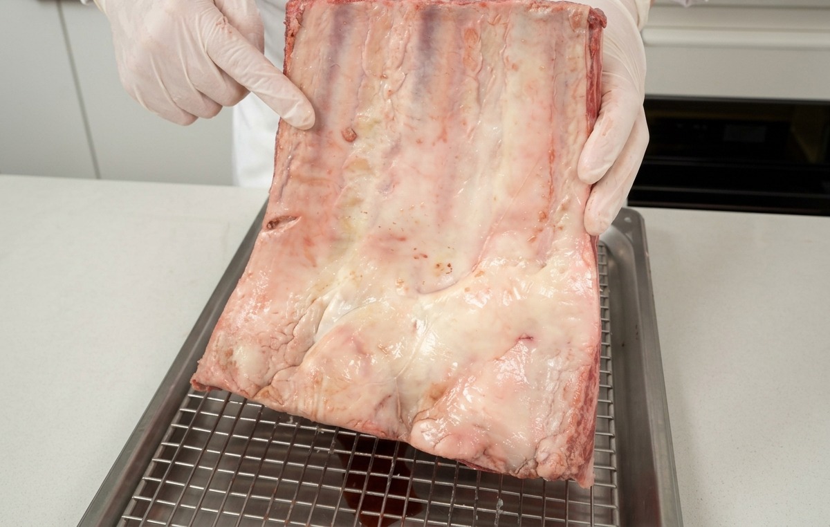 Un chef présentant un morceau de plat de côtes de bœuf cru, montrant le persillage blanc.