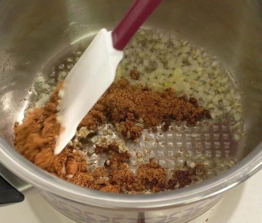 Une spatule mélangeant du sucre roux avec loignon et lail dans une casserole.