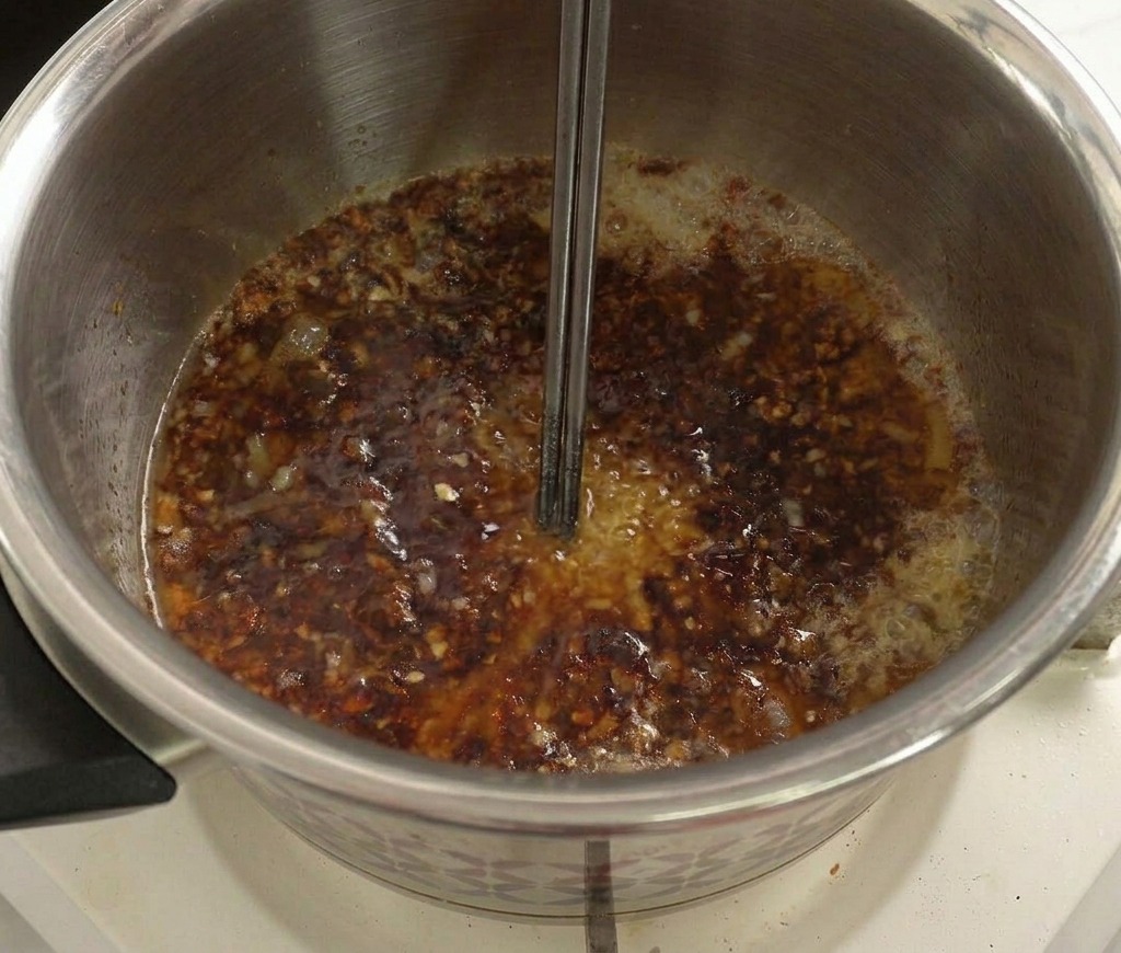 Un mélange liquide sombre bouillonnant dans une casserole, mélangé avec des baguettes en métal.