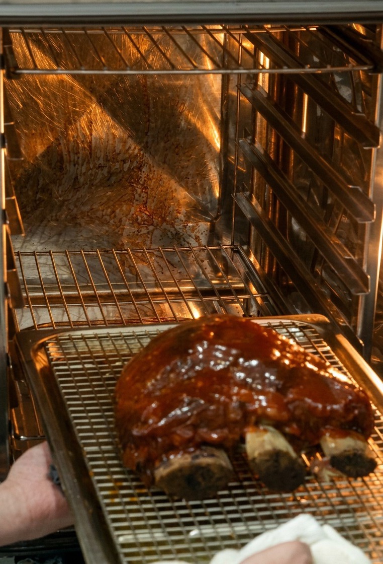 Mains glissant une plaque de cuisson avec les côtes glacées dans un four bien éclairé.