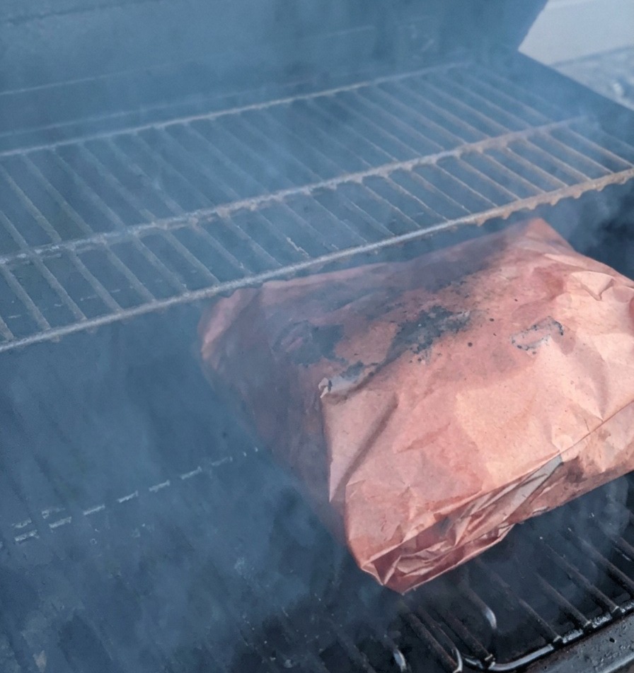 Côtes de bœuf enveloppées dans du papier boucher cuisant sur les grilles du fumoir entourées de fumée.