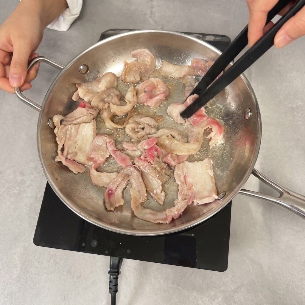 Utilisation dune pince noire pour faire sauter des tranches de poitrine de porc partiellement dorées dans une poêle.