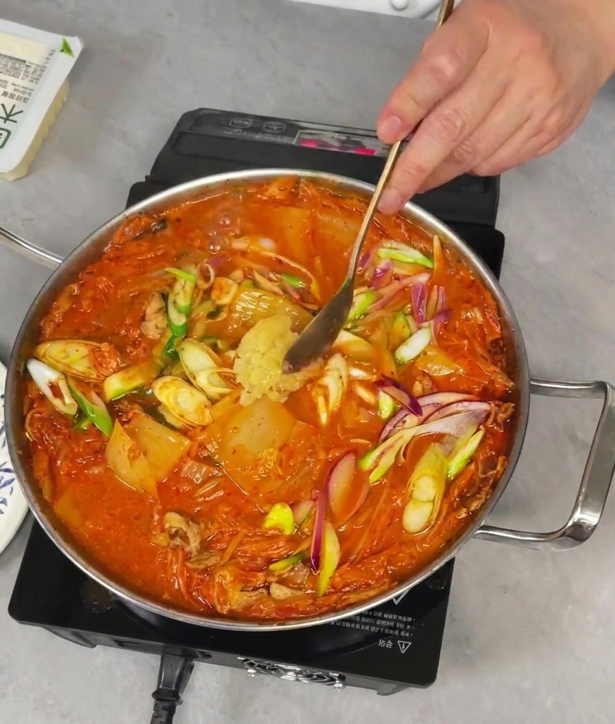 Ajout dune cuillerée dail frais haché dans une poêle bouillonnante de ragoût de kimchi rouge.