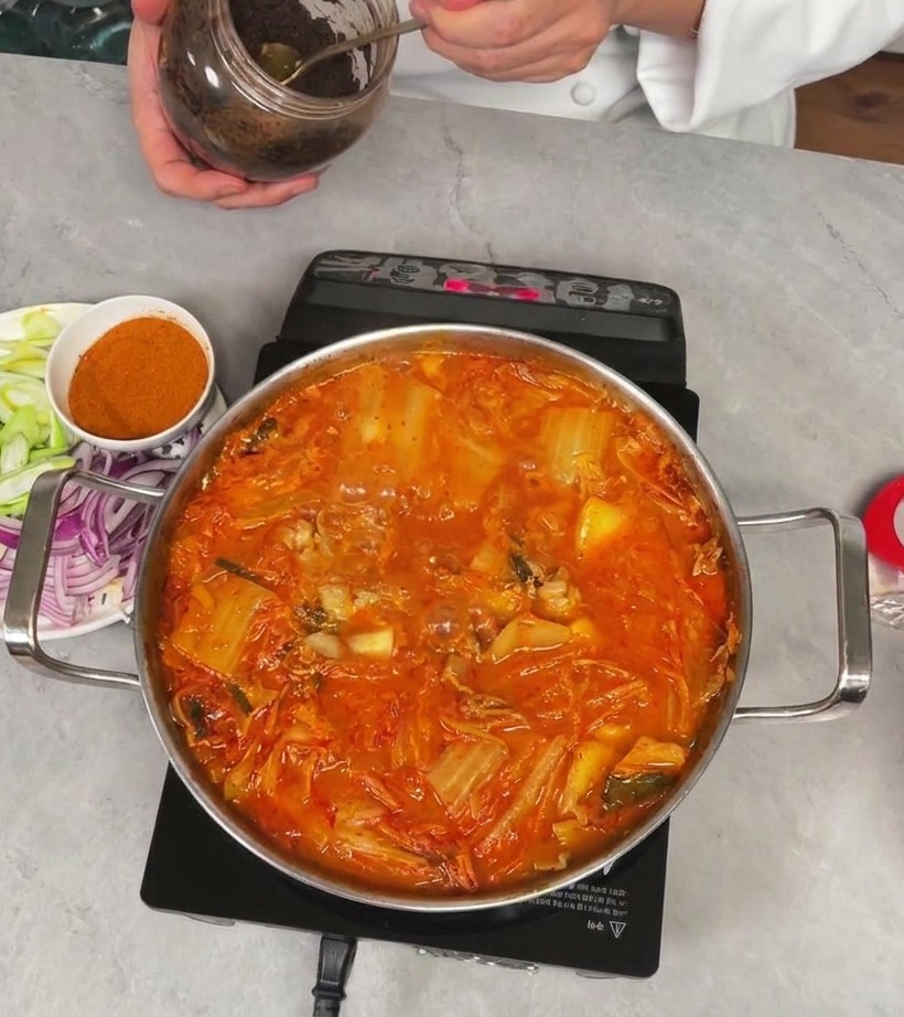 Le chef tient un bocal et prélève une cuillerée de pâte de soja foncée et épaisse pour lajouter au ragoût de kimchi.