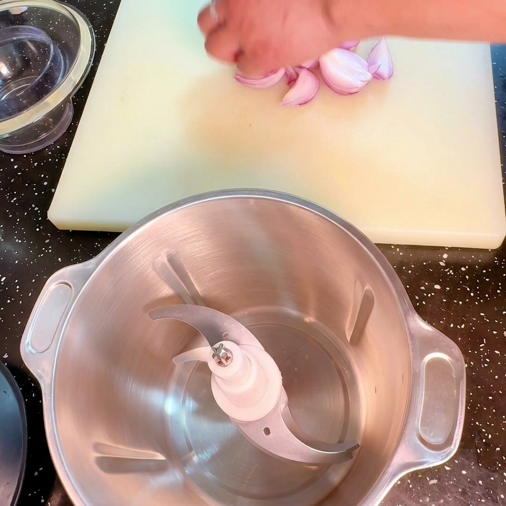 Une main plaçant des morceaux doignon rouge à côté dun robot culinaire sur une planche à découper.