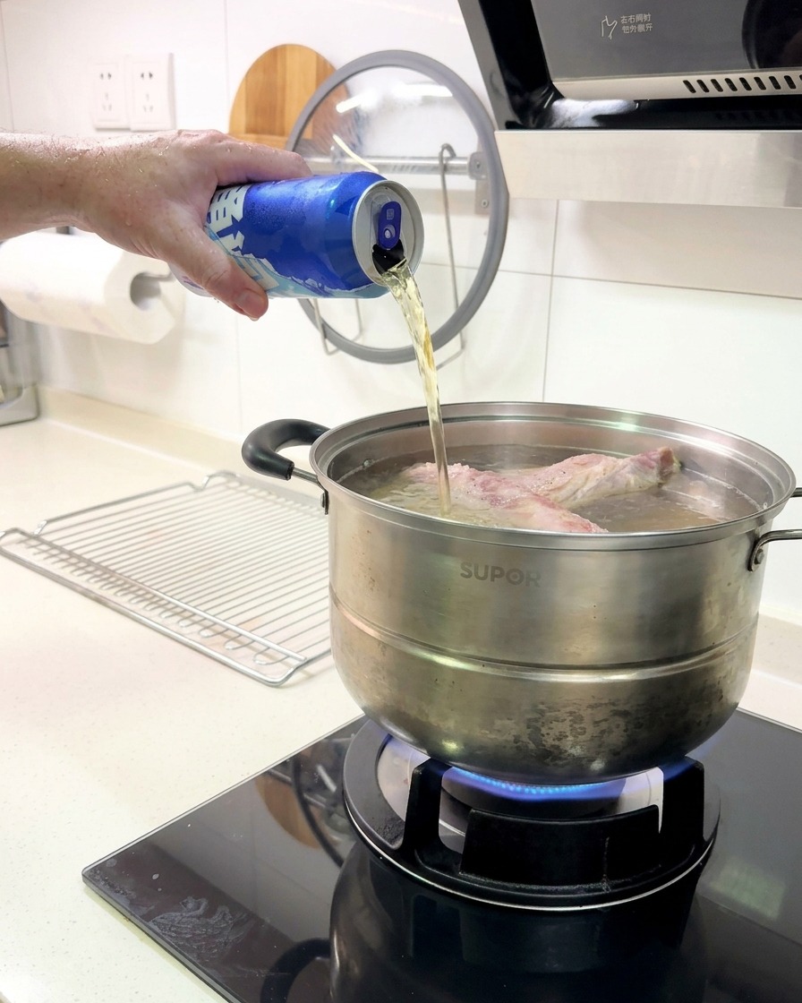Bière versée dune canette bleue dans la marmite contenant les travers de porc.