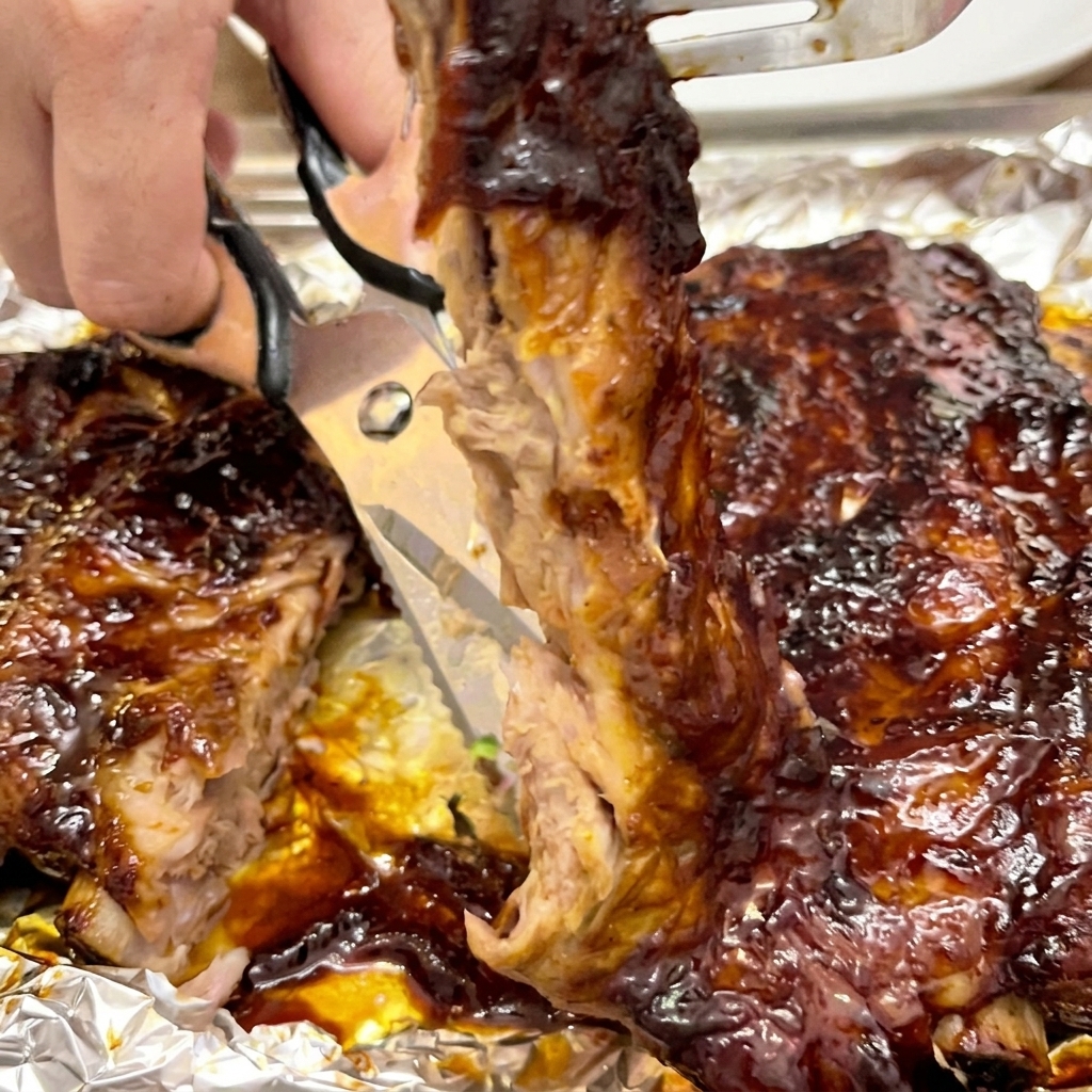 Ciseaux de cuisine coupant entre deux os de ribs recouverts de sauce.