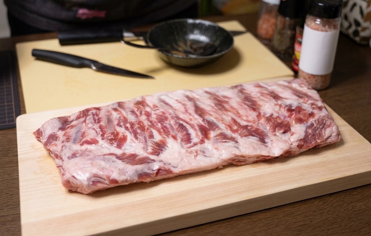 Un travers de porc cru posé sur une planche à découper en bois avec un couteau à côté.