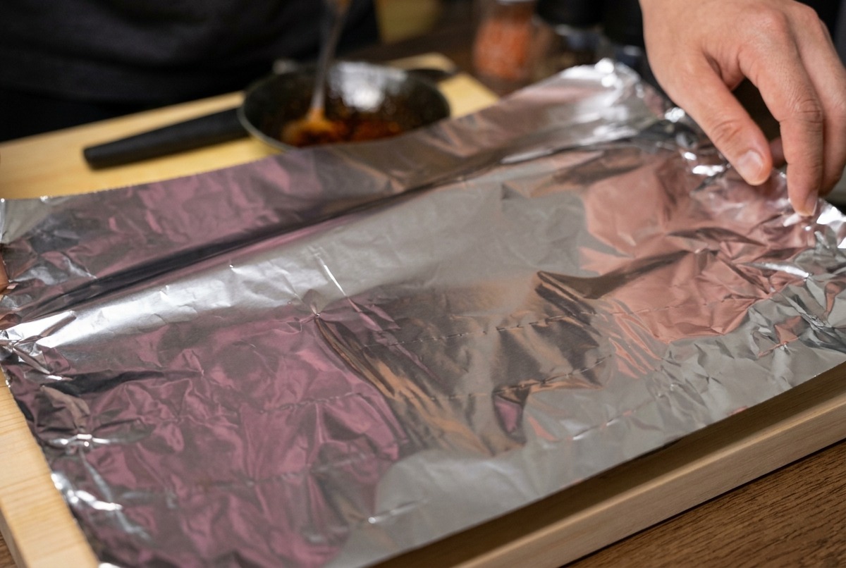 Mains pliant une grande feuille daluminium pour envelopper hermétiquement le travers de porc mariné.