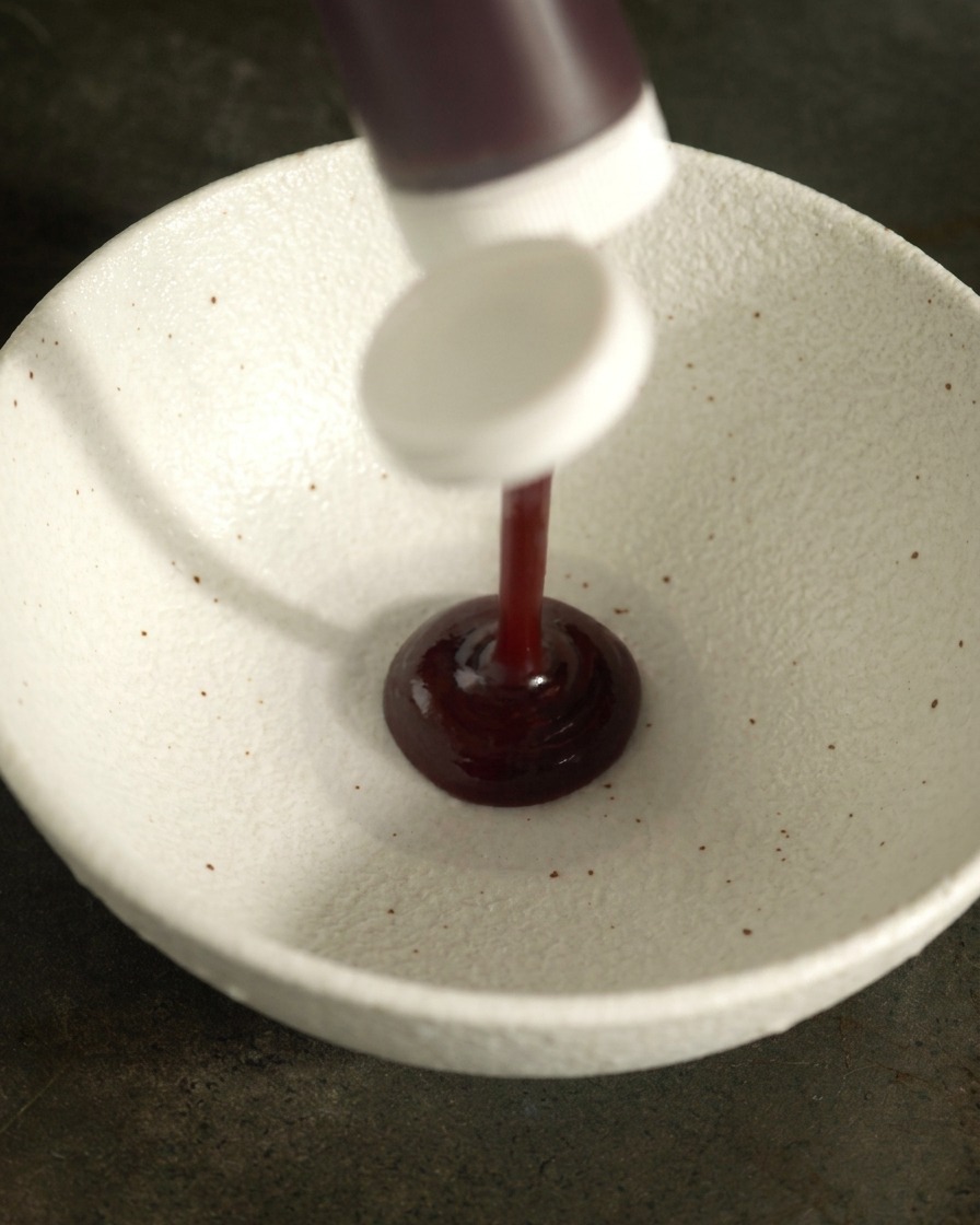Sauce BBQ épaisse et foncée versée dune bouteille dans un bol mélangeur en céramique blanche.