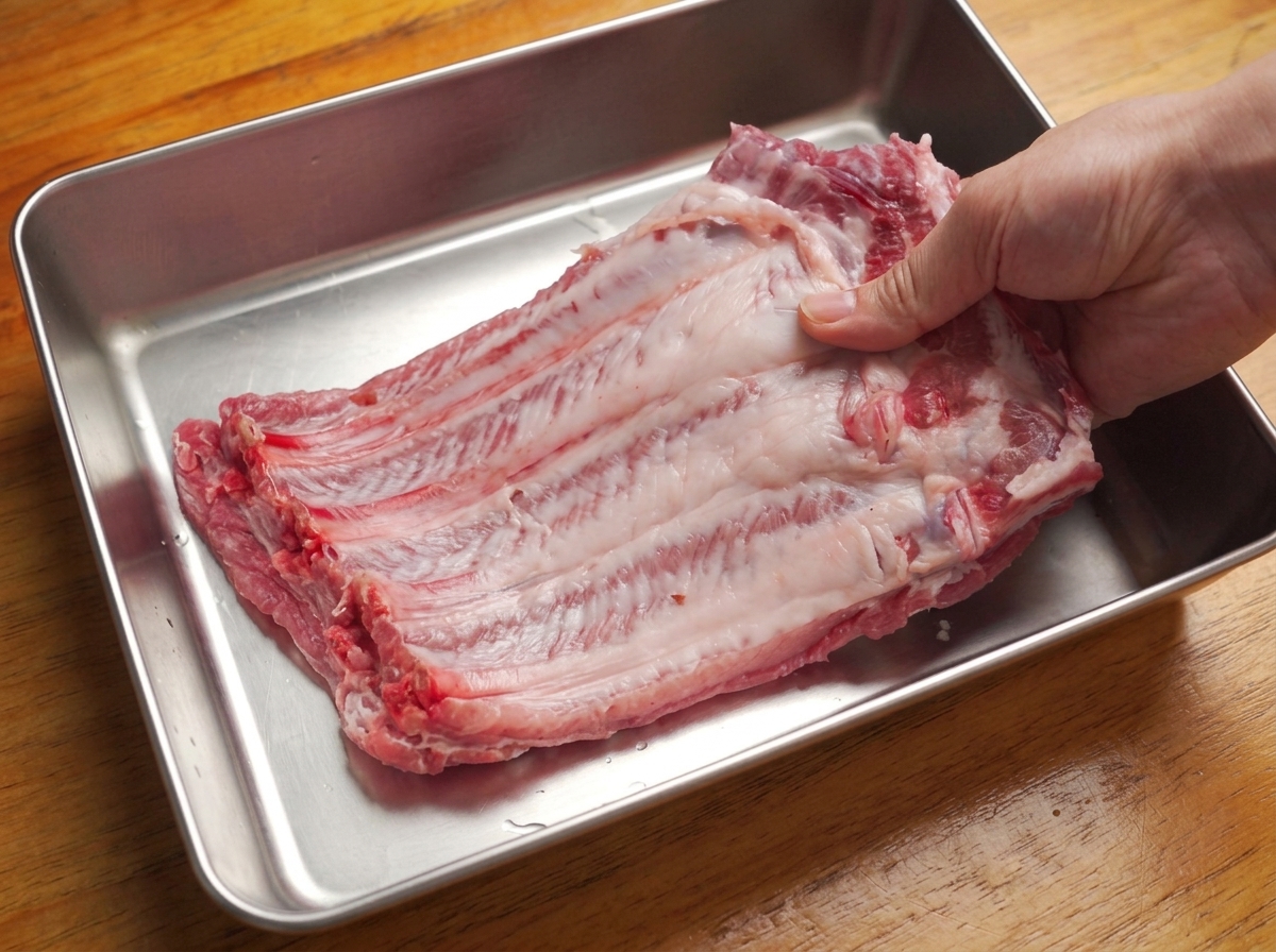 Mains retirant la fine membrane blanche à larrière dun grand carré de travers de porc cru.