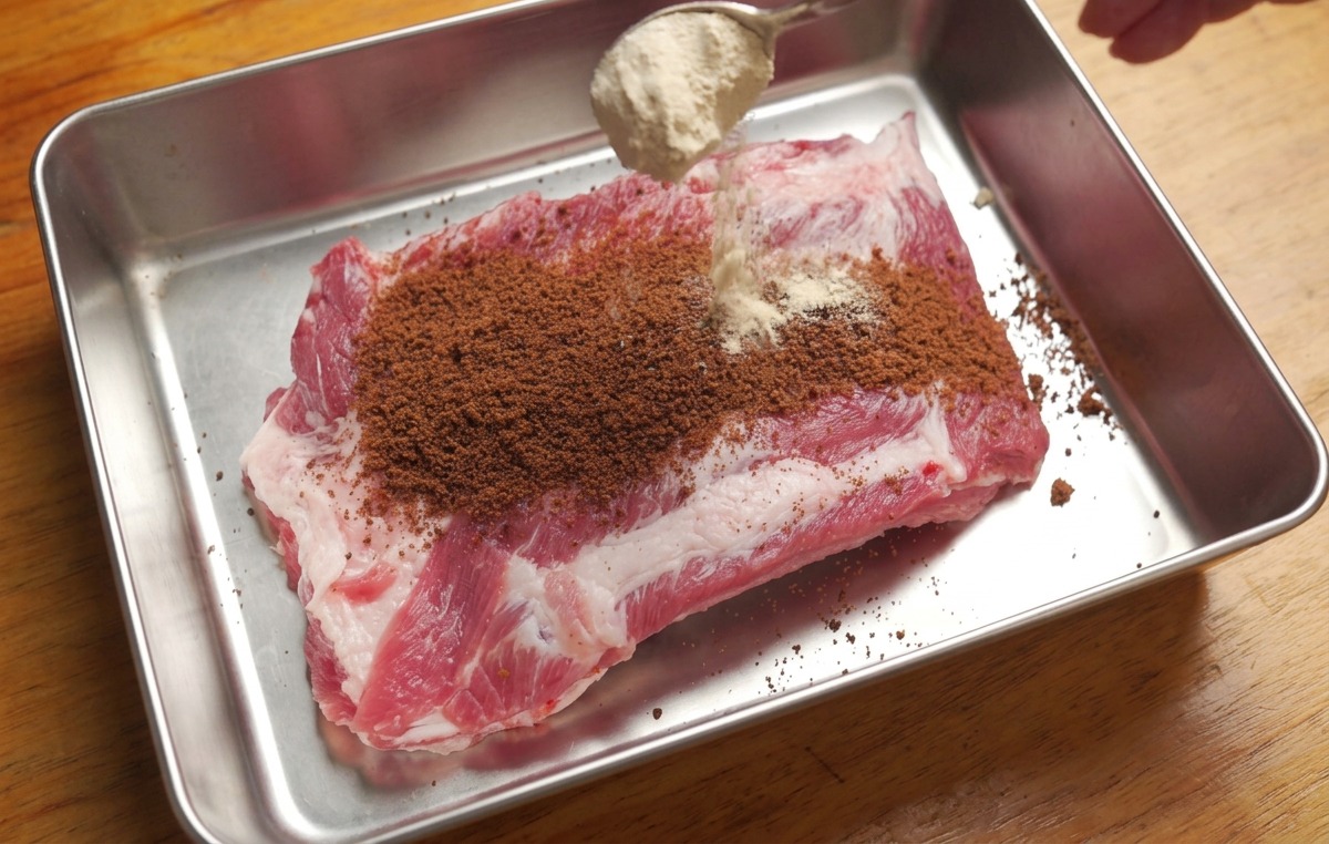 Plateau avec des ribs crus saupoudrés de sucre brun et dun mélange dépices à laide dune cuillère.