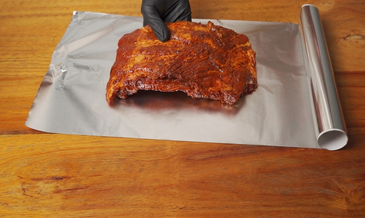 Morceau de travers de porc mariné placé sur une grande feuille de papier aluminium sur une table en bois.