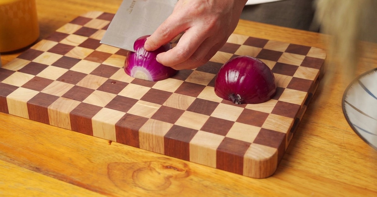 Mains utilisant un couteau pour couper un oignon rouge sur une planche à découper en bois.