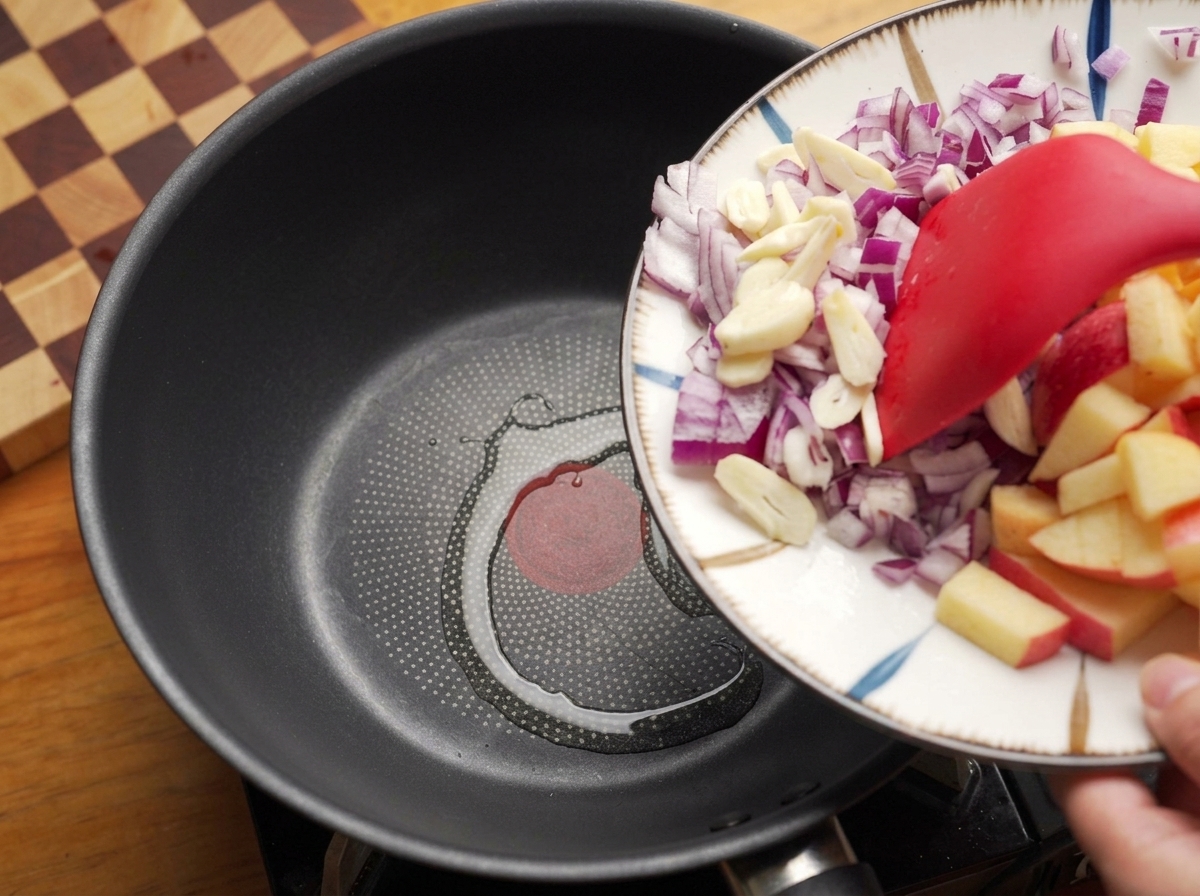 Spatule faisant glisser des oignons rouges et de lail hachés dans une poêle chaude avec de lhuile.