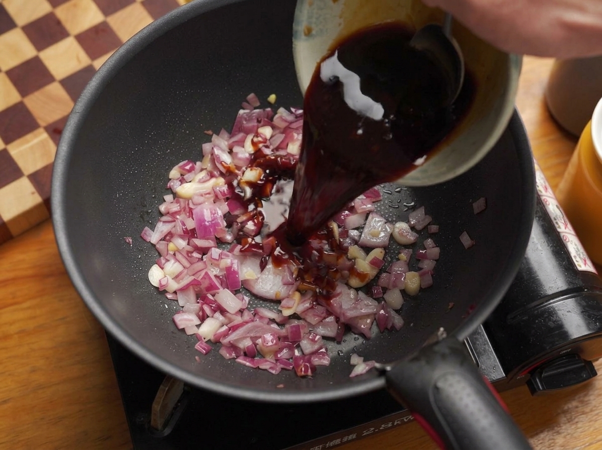 Verser un mélange de sauce sombre et savoureuse dun bol dans une poêle contenant des oignons et de lail.
