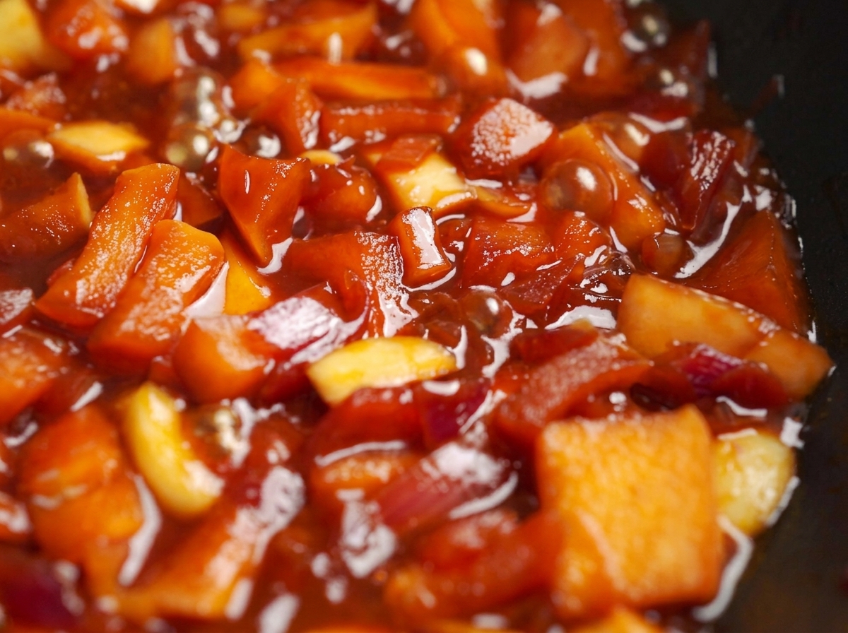 Dés de pommes et oignons mijotant dans une riche sauce rouge dans une poêle.