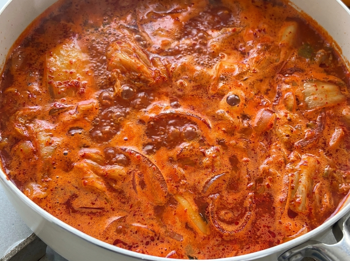Vue de près dune soupe de kimchi rouge vif bouillonnant vigoureusement dans une casserole.