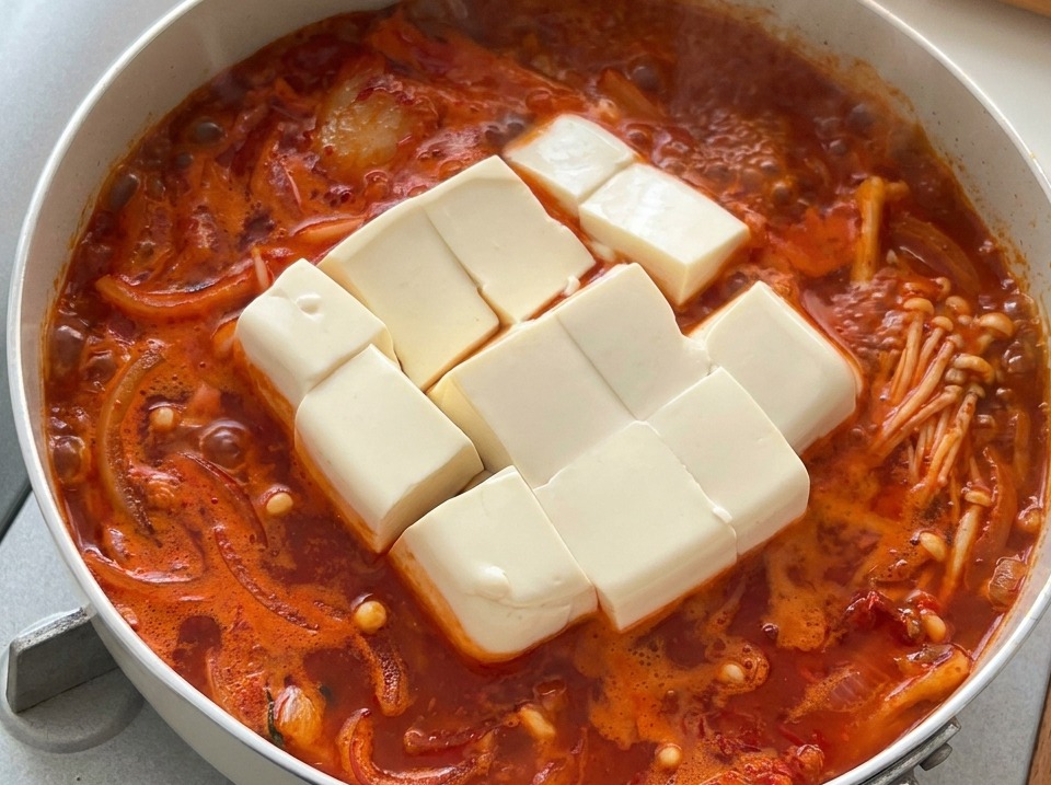 De gros cubes de tofu blanc soyeux dans un ragoût de kimchi coréen chaud et bouillonnant.