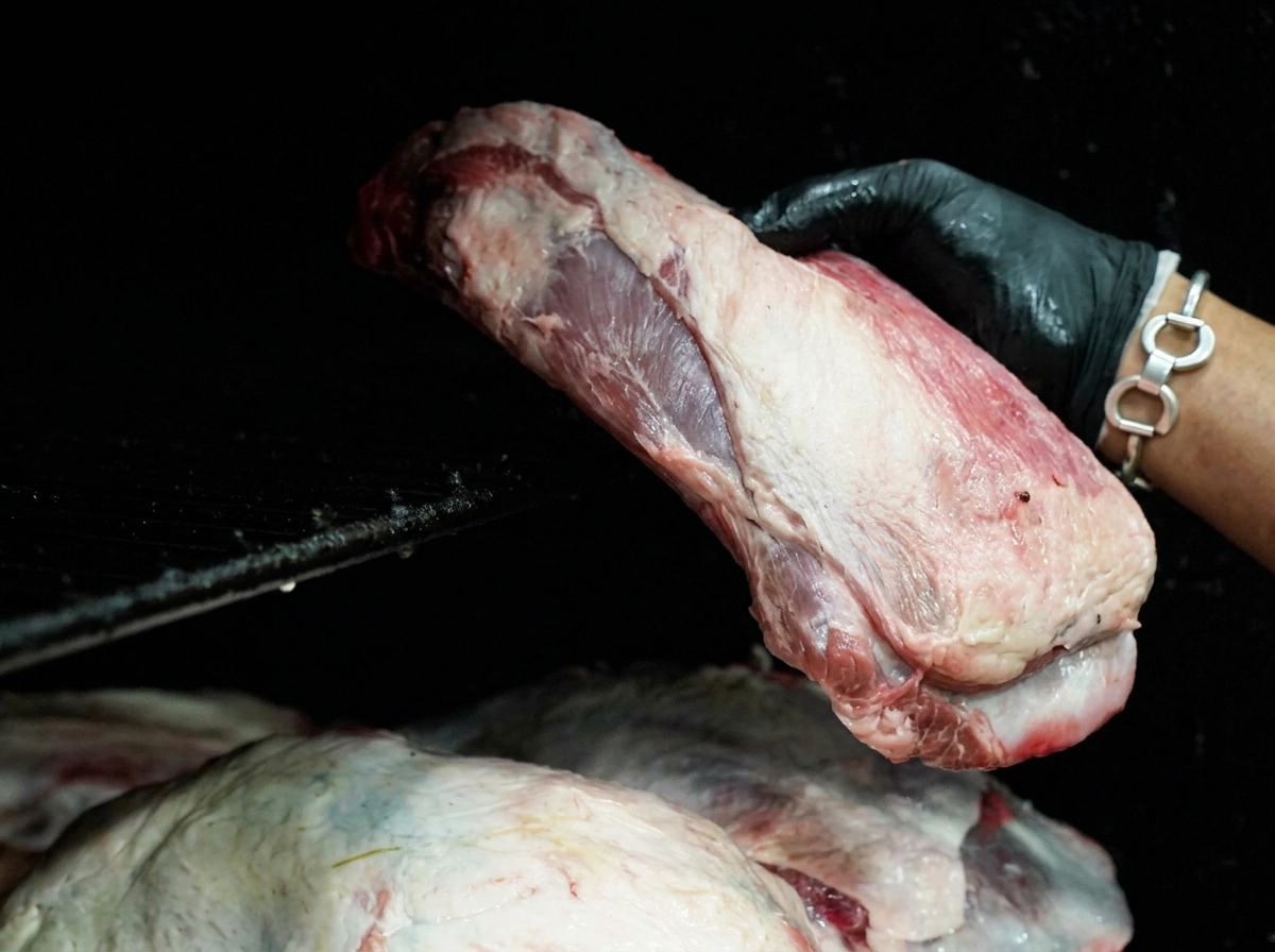 Une main portant un gant noir déposant une large pièce de bœuf crue sur les grilles dun fumoir noir.