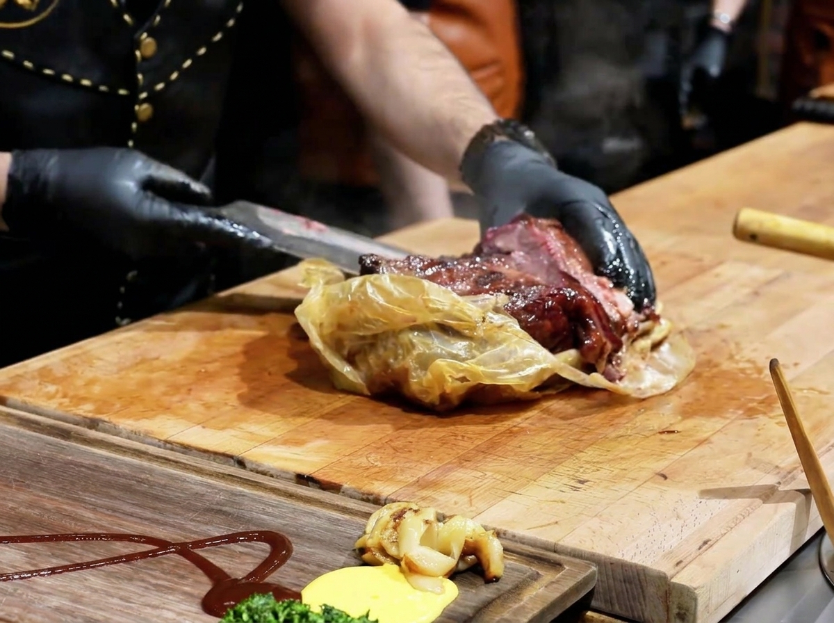 Un chef utilisant un couteau pour ouvrir un emballage de cuisson translucide, révélant une brisket sombre et succulente sur une planche en bois.