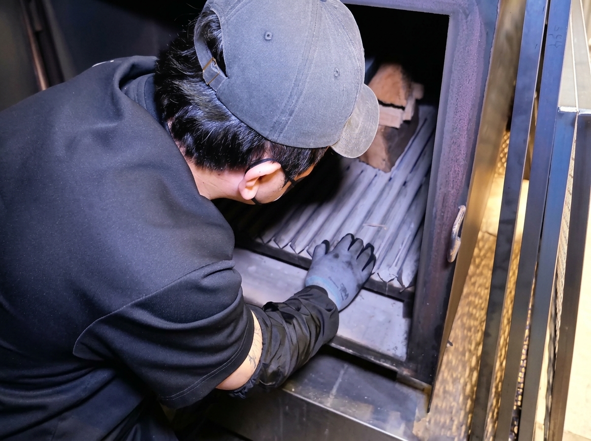 Une personne disposant des bûches de bois à lintérieur du foyer dun grand fumoir en métal.
