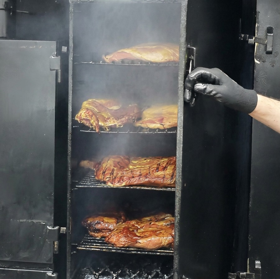 Morceaux de bœuf partiellement fumés et brunis reposant sur les grilles dun grand fumoir ouvert.