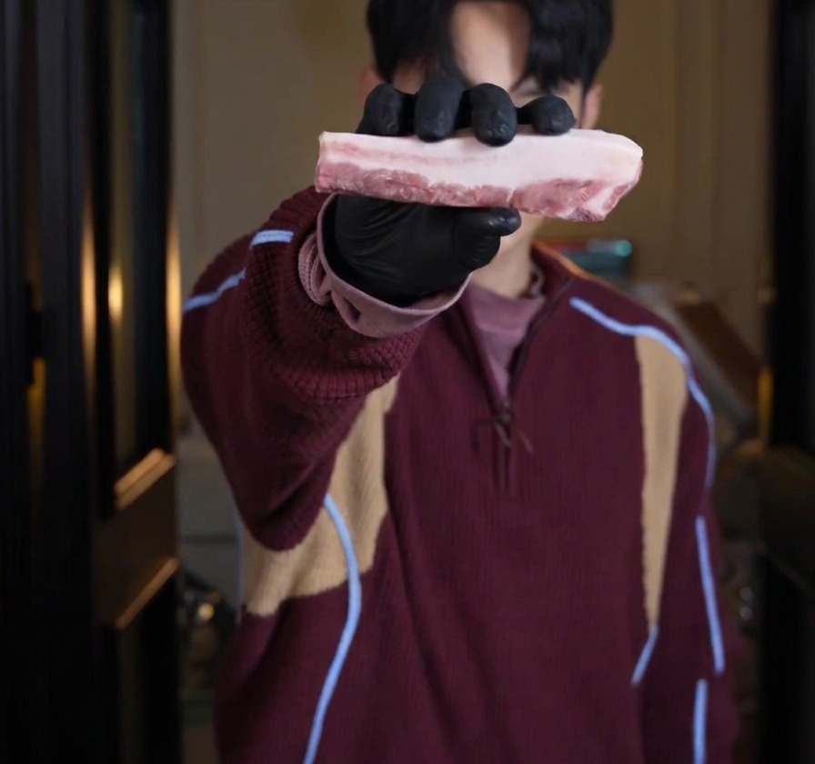 Une personne portant des gants noirs tient un épais morceau cru de poitrine de porc striée.