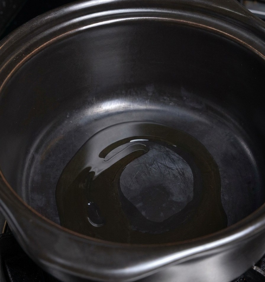 Une fine couche dhuile de cuisson miroitant au fond dune marmite en céramique foncée et chauffée.