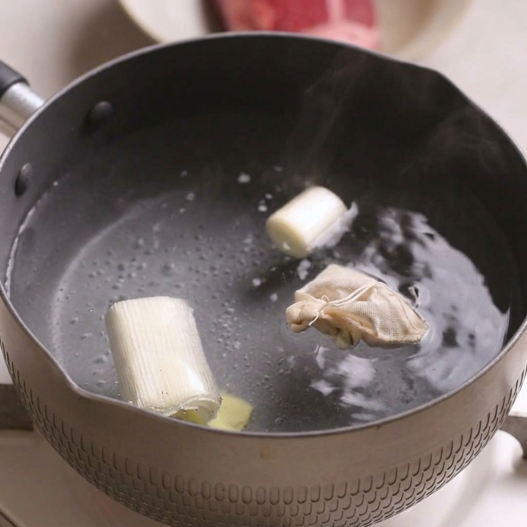Une petite casserole deau bouillante contenant des morceaux doignons verts, une tranche de gingembre et un petit sachet dépices.