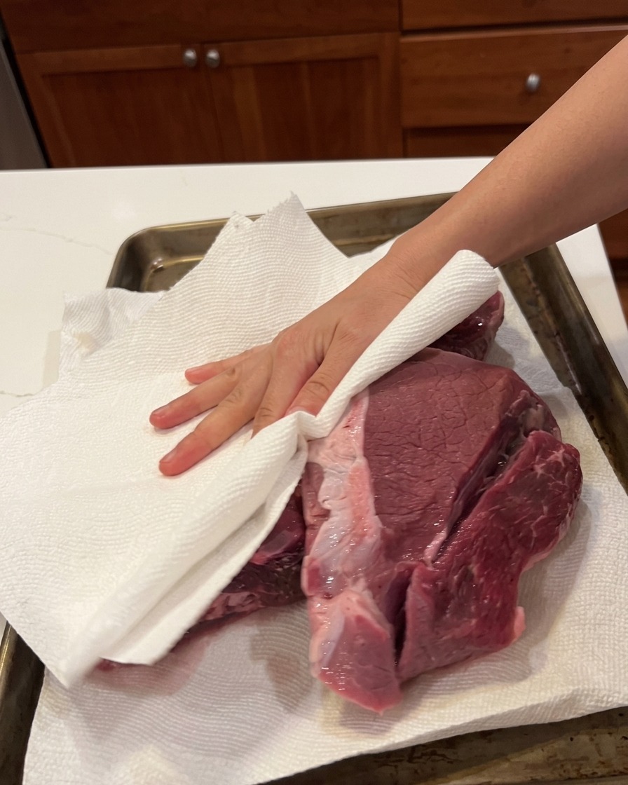 Une main utilisant du papier absorbant pour sécher une grande pièce de bœuf cru.