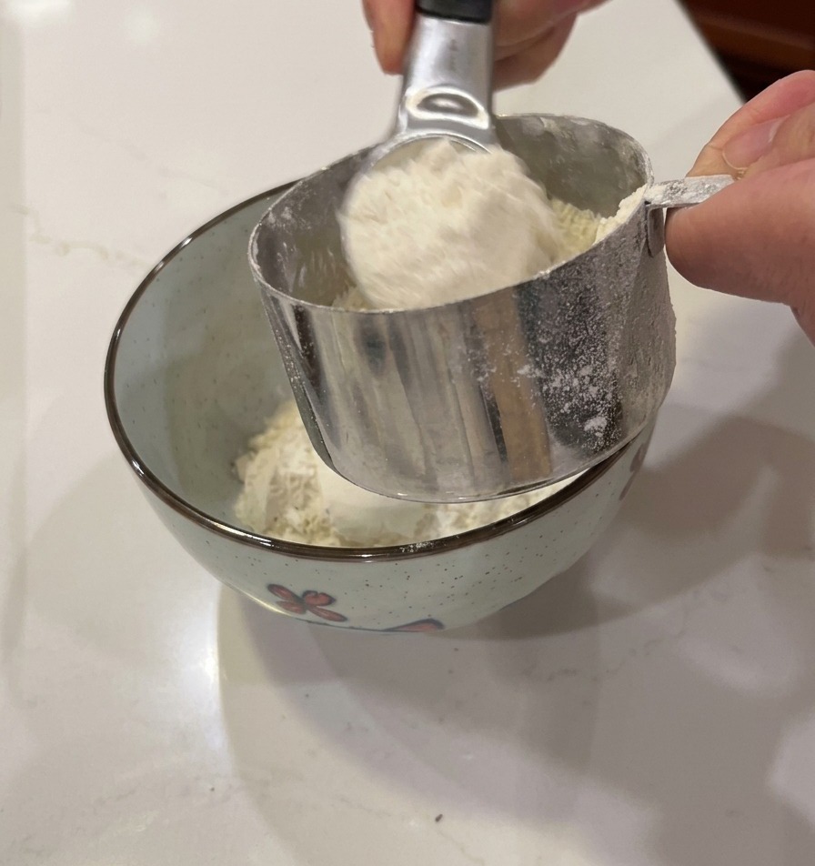 Mains versant de la farine blanche dun gobelet doseur dans un petit bol.