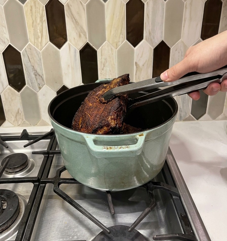 Morceaux de bœuf saisis transférés avec une pince dans une cocotte en fonte verte.