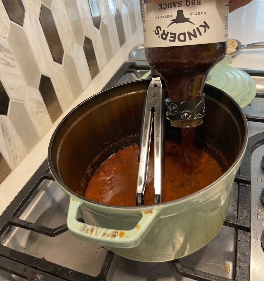 Versement dune bouteille de sauce BBQ dans la cocotte contenant le jus de cuisson réduit.