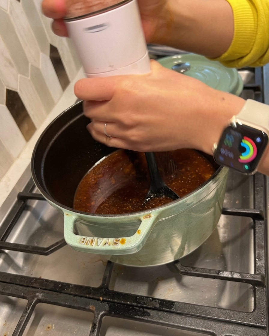 Un moulin électrique versant du sel et du poivre dans la sauce fumante.