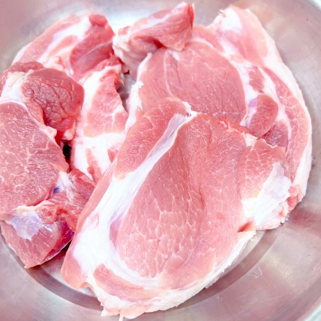 Morceaux épais dépaule de porc crue placés dans un bol en acier inoxydable.