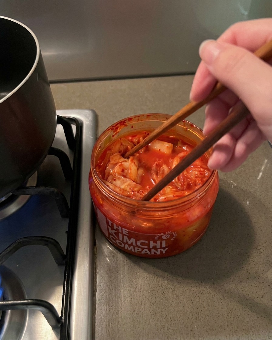 Des baguettes en bois soulevant du kimchi rouge épicé dun bocal en plastique transparent.