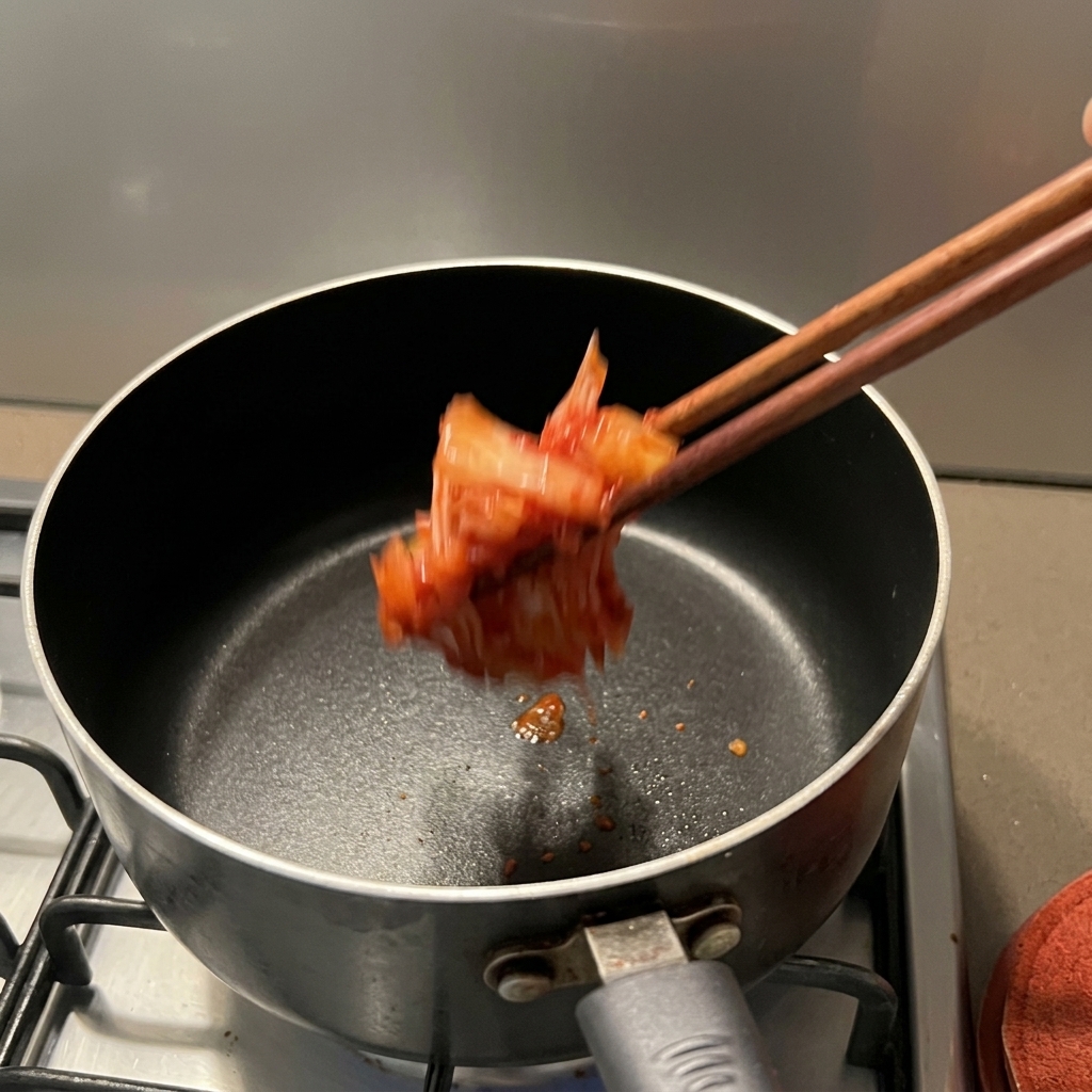 Du kimchi rouge assaisonné déposé dans une casserole antiadhésive foncée sur une cuisinière.