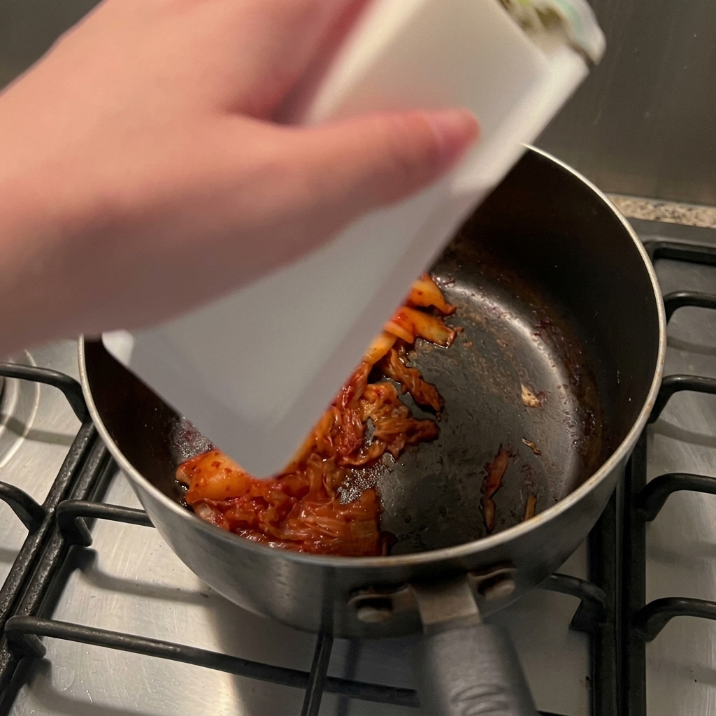 Un bloc de tofu soyeux blanc glissant de son emballage dans une casserole contenant le kimchi sauté.