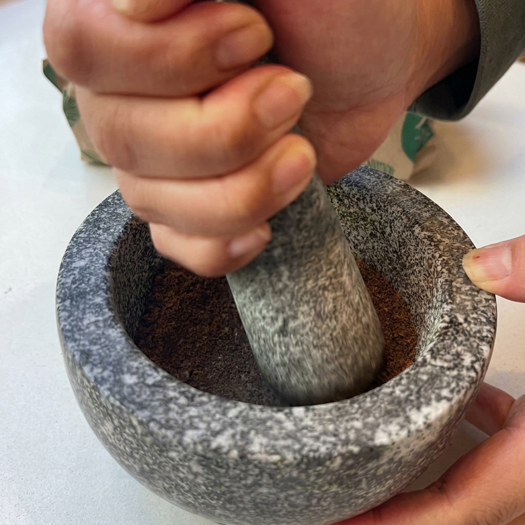 Mains utilisant un pilon pour écraser des épices torréfiées en une poudre fine dans un mortier en granit.