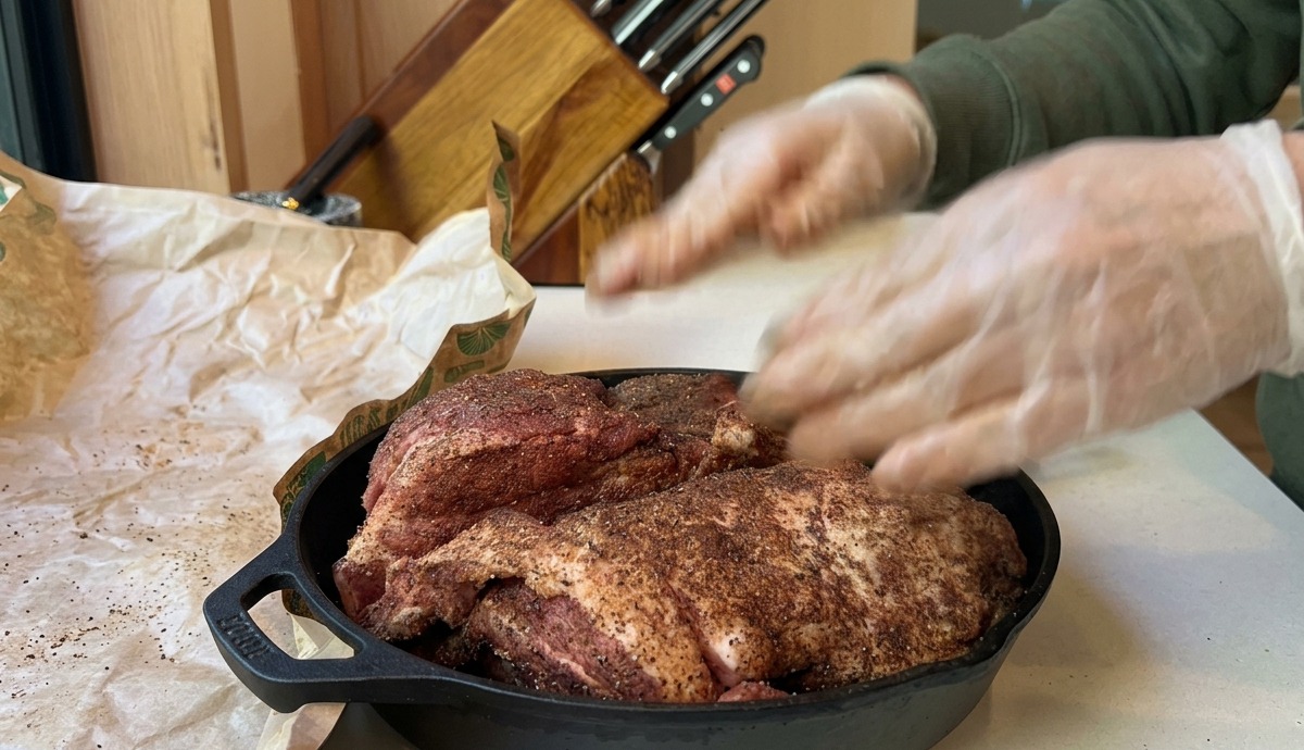 Une épaule de porc assaisonnée dans une poêle en fonte, prête à être enfournée.