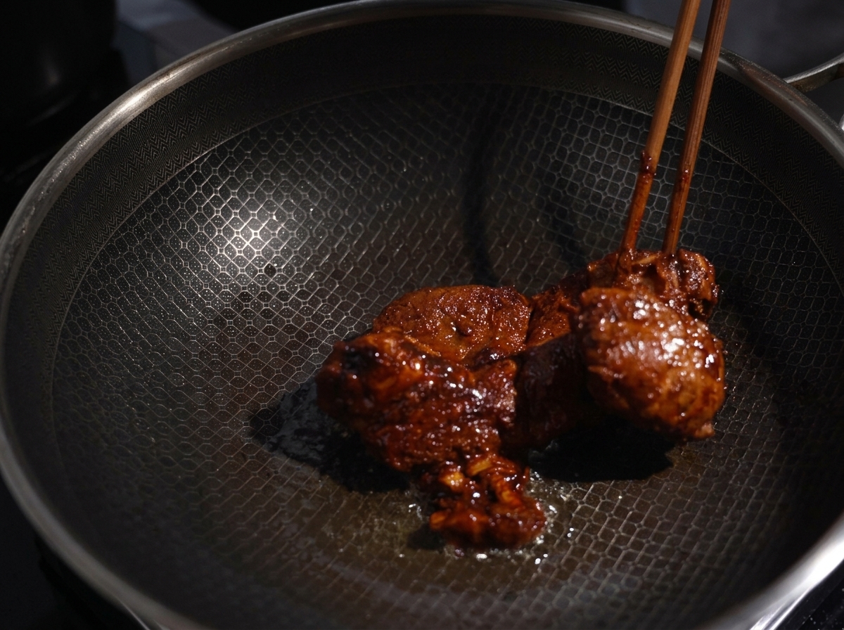 Morceaux de porc saisis dans un wok chaud avec des baguettes, montrant une croûte bien dorée.