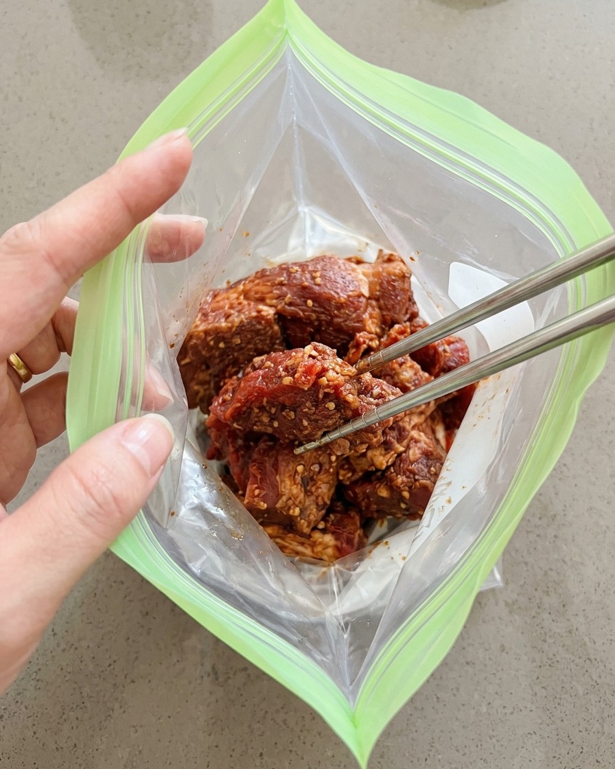 Morceaux de porc épicés placés dans un sac de congélation réutilisable avec des baguettes.