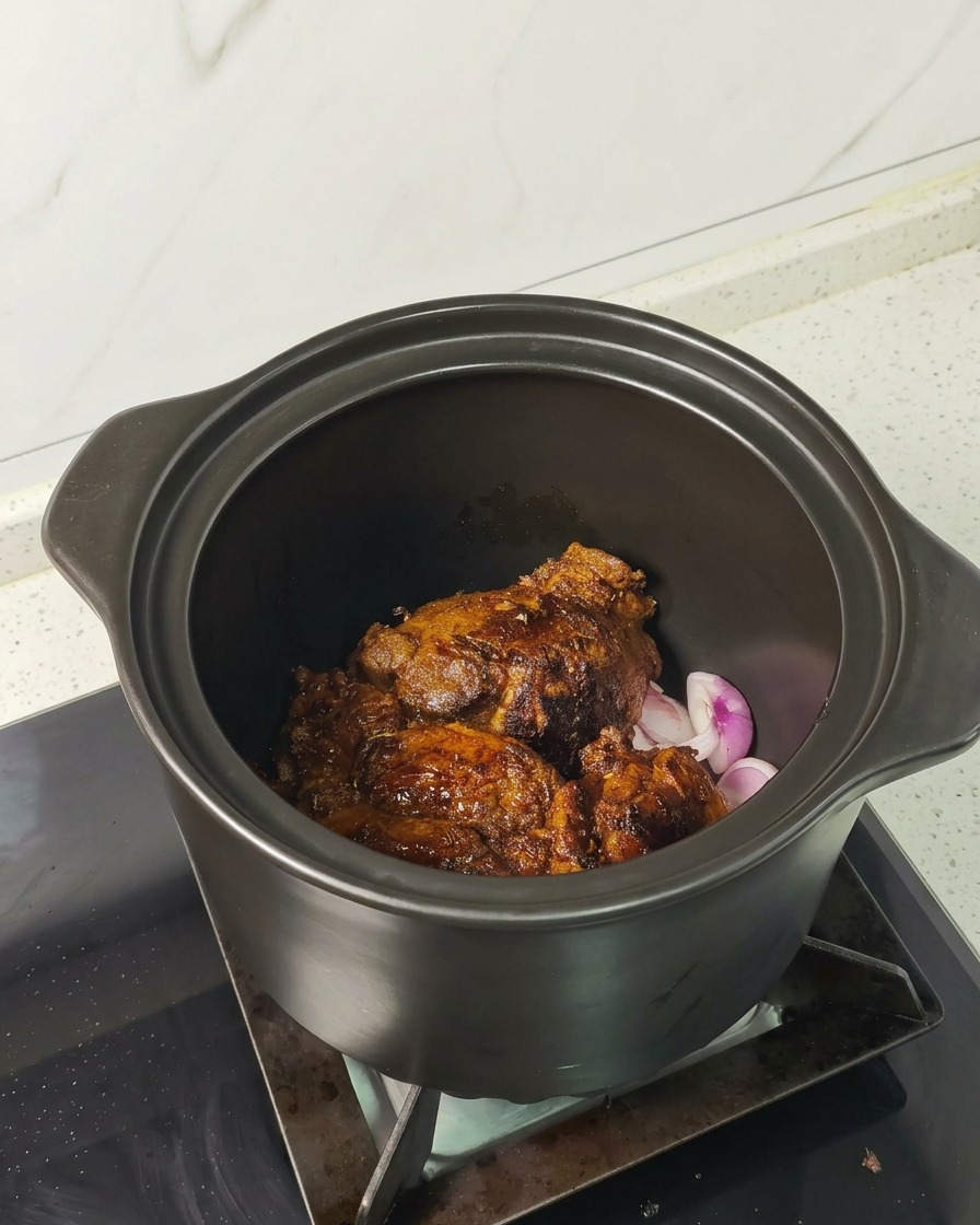Morceaux de porc bien dorés reposant sur des échalotes dans une cocotte en céramique.